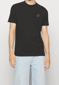 T-shirt in cotone nero con scollatura rotonda e maniche corte, caratterizzato da un delicato ricamo grafico sul lato sinistro del petto.
