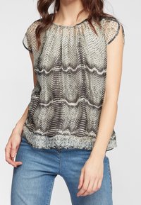 Kortärmad topp med ett ormskinsmönster i nyanser av grått och krämvitt, med ett genomskinligt tyg och en rundad halsringning.