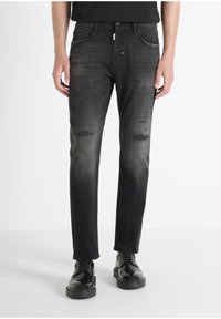 Vaqueros de denim negro con áreas desgastadas y detalles deshilachados. Diseño de pierna recta, estilo de cinco bolsillos, combinados con zapatos negros pulidos.