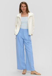 Weiße Zip-Jacke, blaue weit geschnittene Hose, gestreiftes helles Oberteil. Glatte Texturen, lässiges Design, entspannter Schnitt. Keine auffälligen Muster oder Akzente.
