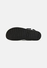 Black rubber shoe sole featuring a wavy pattern for grip, with a slightly raised heel and a smooth, textured finish.