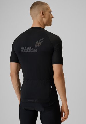 Mężczyzna ubrany w czarną sportową koszulkę z krótkim rękawem z logo "GET LOST. FEEL FOUND." i "4F" na plecach, twarzą odwrócony.