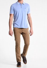 Polo shirt azzurro chiaro con colletto bianco, maniche corte e taschino sul petto; abbinato a pantaloni chinos slim-fit beige e sneakers marrone scuro.