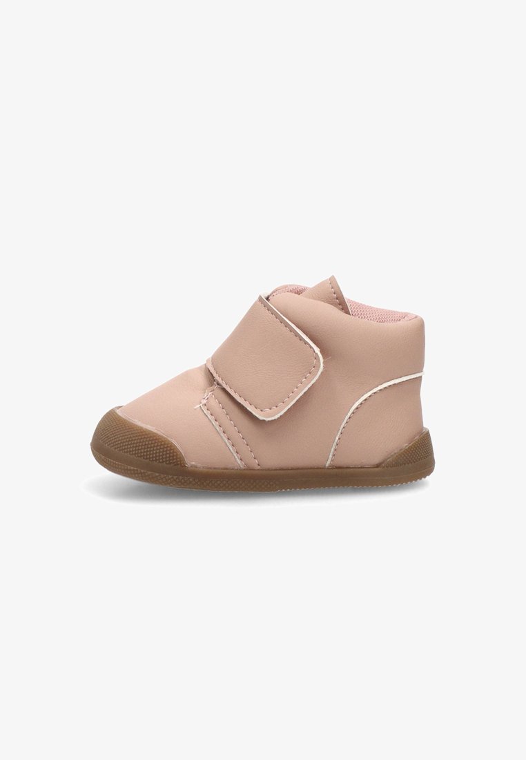 Bota de tobillo de cuero rosa con una correa de velcro, punta redondeada y suela de goma marrón. Presenta costuras blancas y una superficie texturizada.