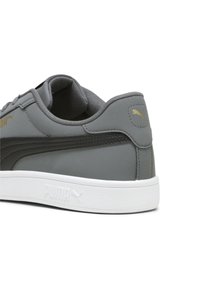 Szürke sneaker szintetikus felsőrésszel, fehér gumitalppal, párnázott bokával és arany logó részletekkel. Simább textúrával és lekerekített formával rendelkezik.