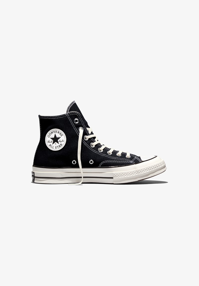 Baskets montantes Converse All Star noires avec semelle en caoutchouc blanche, lacets blancs et écusson rond avec logo à la cheville.