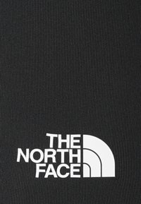 Tissu noir côtelé arborant un logo blanc bien visible de "The North Face" avec un design en arc, positionné dans la section inférieure.