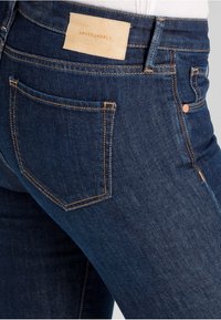 Tmavě modré džíny z denimu s hladkou texturou, s zadní kapsou a hnědou koženou etiketou s vyraženým nápisem "ARMEDANGELS".