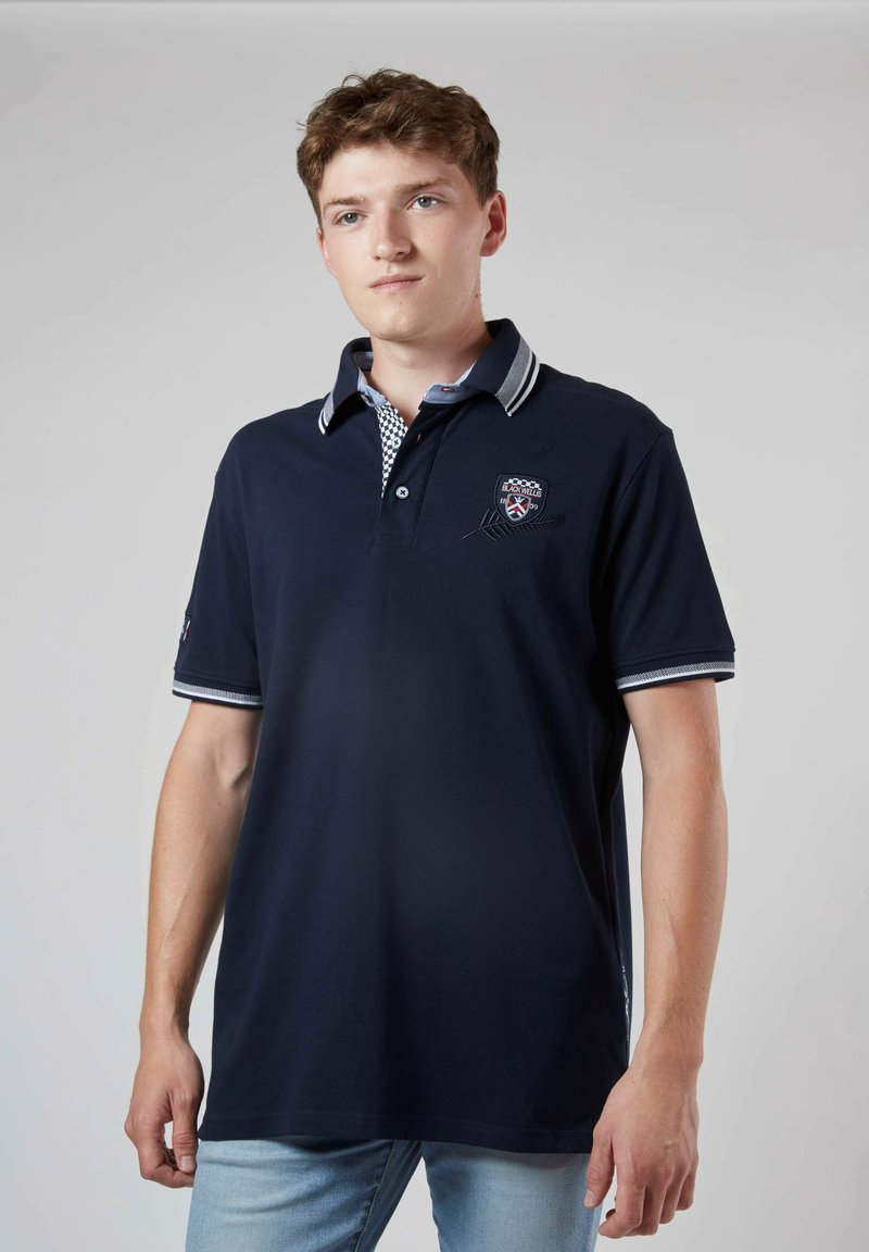 Polo marine à manches courtes, avec un col à carreaux contrastés, un logo brodé et des accents rayés sur les manches.