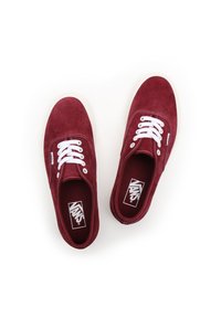 Zapatillas de ante rojas con cordones blancos, un diseño de corte bajo y una suela de goma blanca. El interior presenta un forro burdeos a juego.