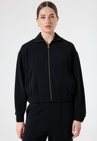 Schwarze Zip-Jacke mit hohem Kragen, gerippten Bündchen und Saum; verfügt über eine glatte Textur und ein Raglan ärmel Design.