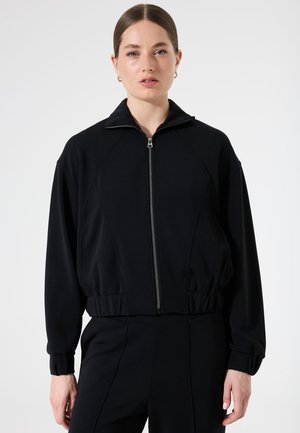 Veste noire zippée avec un col haut, des poignets et une taille côtelés ; présente une texture lisse et un design à manches raglan.
