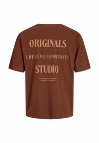 Camiseta de algodón marrón con un corte relajado. Presenta un gran texto en un tono más claro que dice "ORIGINALS", "CREATIVE COMMUNITY" y "STUDIO".