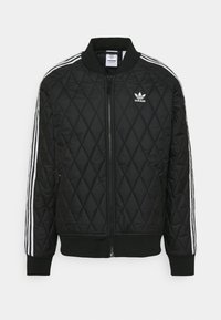 Svart vadderat bomberjacka med ribbade ärmslut och nederkant, med vita tre-stripes detaljer på ärmarna och en broderad logotyp på bröstet.