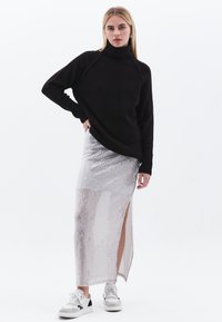 Zwarte gebreide coltrui, zilveren paillettenrok met hoge split en witte sneakers met zwarte accenten. Eenvoudig ontwerp; textuurafwerking.