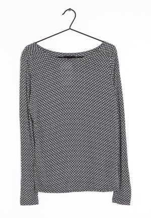 Haut à manches longues noir et blanc avec un petit motif géométrique suspendu à un cintre en fil noir sur fond blanc.