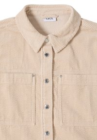 Béžová kordurová košile s límečkem, zajímavým zapínáním na knoflíky, dvěma chest kapsami a stříbrnými knoflíky s texturovaným povrchem.