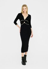 Czarna dopasowana sukienka z długimi rękawami, głębokim dekoltem w serek i złotym akcentem w talii. Modelka zestawiła ją z czarnymi wojskowymi butami. Prosty design.
