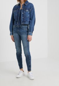 Zkrácená džínová bunda s knoflíkovým zapínáním, modré džíny s vyšívanými detaily a bílé tenisky. Ležérní outfit v odstínech modré.