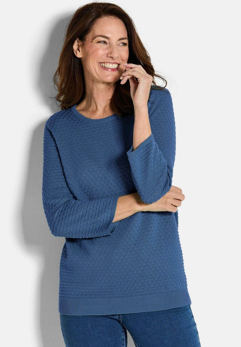 Blauer strukturierter Pullover mit Dreiviertelärmeln, geripptem Saum und rundem Halsausschnitt, kombiniert mit Jeans. Weicher Strickstoff mit Details.