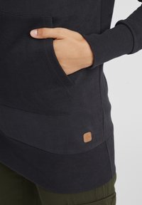 Felpa di un oscuro blu navy con tasca frontale, polsini a coste e tessuto testurizzato. Un piccolo etichetta beige è visibile sul lato sinistro in basso.
