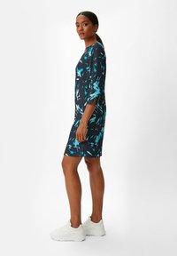 Korte mouwen jurk van marineblauwe stof met turkooise abstracte patronen; knie-lengte, aangesloten silhouet, gecombineerd met witte sneakers.