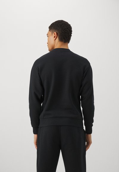 Sudadera negra de tela gruesa, con cuello redondo, mangas largas y puños y dobladillo de canalé. Textura suave sin patrones visibles.
