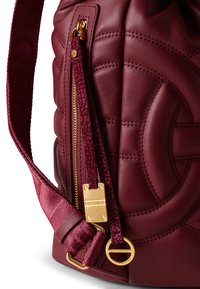 Burgundy leather bag with quilted texture, gold hardware, a zip pocket, and a patterned strap. Features a ring attachment detail.
