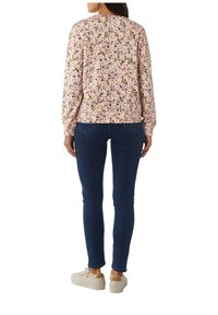 Roze sweatshirt met bloemenpatroon, lange mouwen, ribgebreide boorden en zoom, gecombineerd met donkere skinny jeans en beige sneakers.