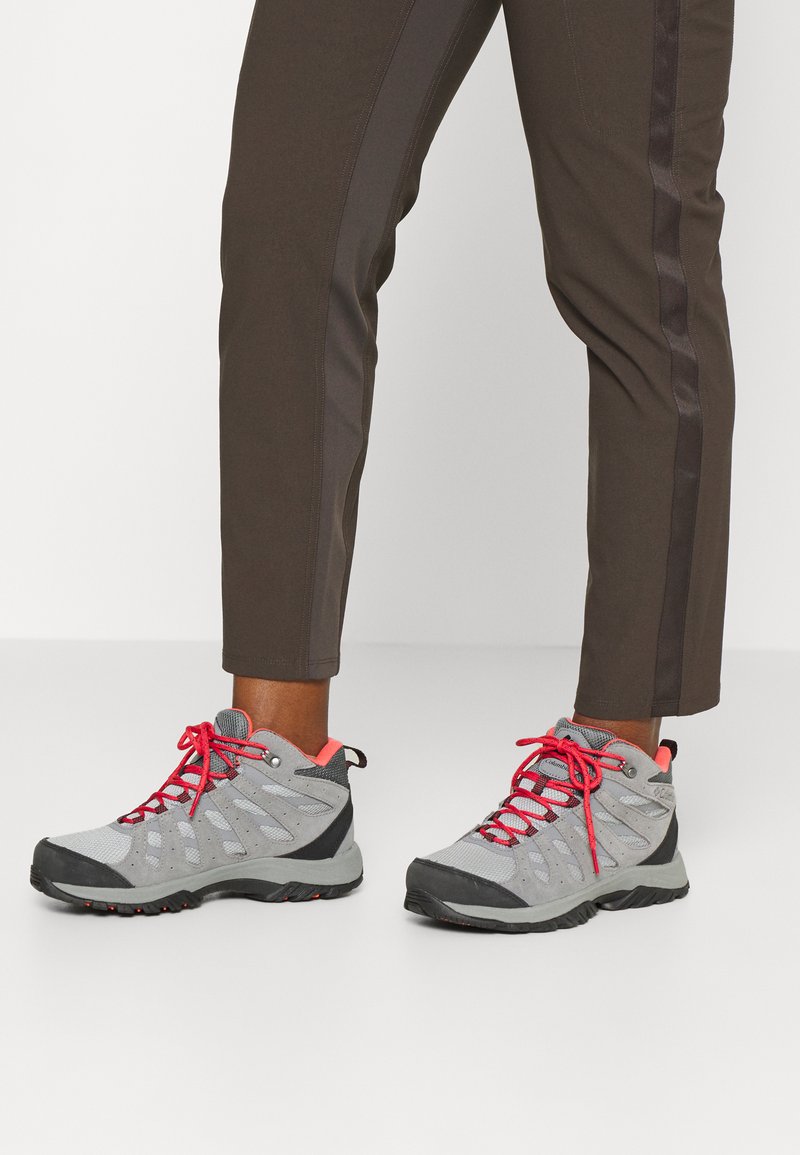 Grau Wanderschuhe mit roten Schnürsenkeln und Akzenten. Obermaterial aus Mesh mit Gummisohle, Hochschnitt-Design und seitlichen Belüftungsdetails.