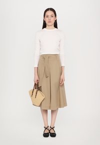 Beige indpakningsskørt med en bindebånd, parret med en hvid langærmet bluse. Sorte sko med krydset remme. Holder en lille vævet håndtaske.