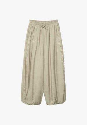 Luźne, beżowe spodnie o szerokich nogawkach z elastycznym pasem, sznurkiem do wiązania, bocznymi kieszeniami i ozdobnymi ćwiekami wzdłuż zewnętrznych szwów.