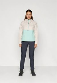 Lichtgewicht, geïsoleerd jack met een lichtbeige bovenkant en een muntgroene onderkant. Gecombineerd met donkere, aansluitende broek en zwarte wandelschoenen.