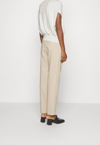 Beige kalhoty s vysokým pasem a uvolněným střihem, doplněné světle šedým topem s krátkým rukávem. Vzhled doplňují černé muly na blokovém podpatku.