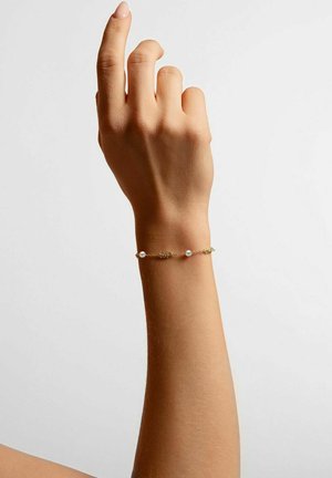 Goldene Gliederarmband mit zwei kleinen Perlen, mit einem zarten, strukturierten Design. Getragen an einer teilweise erhobenen Hand vor einem neutralen Hintergrund.