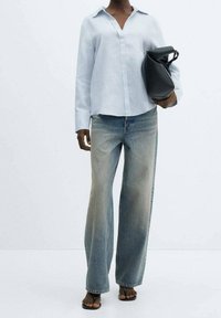 Chemise bleue claire à manches longues avec un décolleté en V, assortie à un jean en denim bleu délavé à jambes larges et un sac à main noir. Des sandales plates complètent le look.