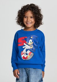 Felpa blu con una grande grafica di Sonic the Hedgehog, con accenti rossi. Realizzata in materiale morbido, con polsini e orlo a coste.