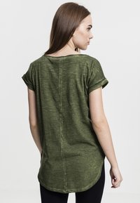 Camicia corta a maniche corte verde oliva con una vestibilità rilassata, polsini arrotolati e orlo arrotondato. Tessuto texturizzato con un delicato motivo a righe.