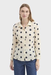 Chemise crème boutonnée avec de gros pois bleu marine, manches longues et col à revers. Le tissu semble léger et texturé.