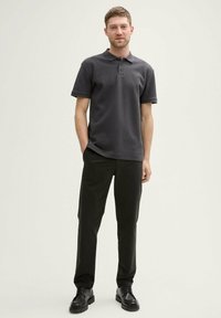 Grå poloshirt med tekstureret finish, tre-knaps placket og korte ærmer, parret med sorte bukser og sorte sko.