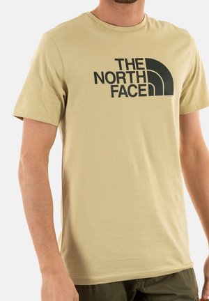 Beige cotton t-shirt featuring a large black logo of "The North Face" on the front. Crew neck and short sleeves with a smooth texture.