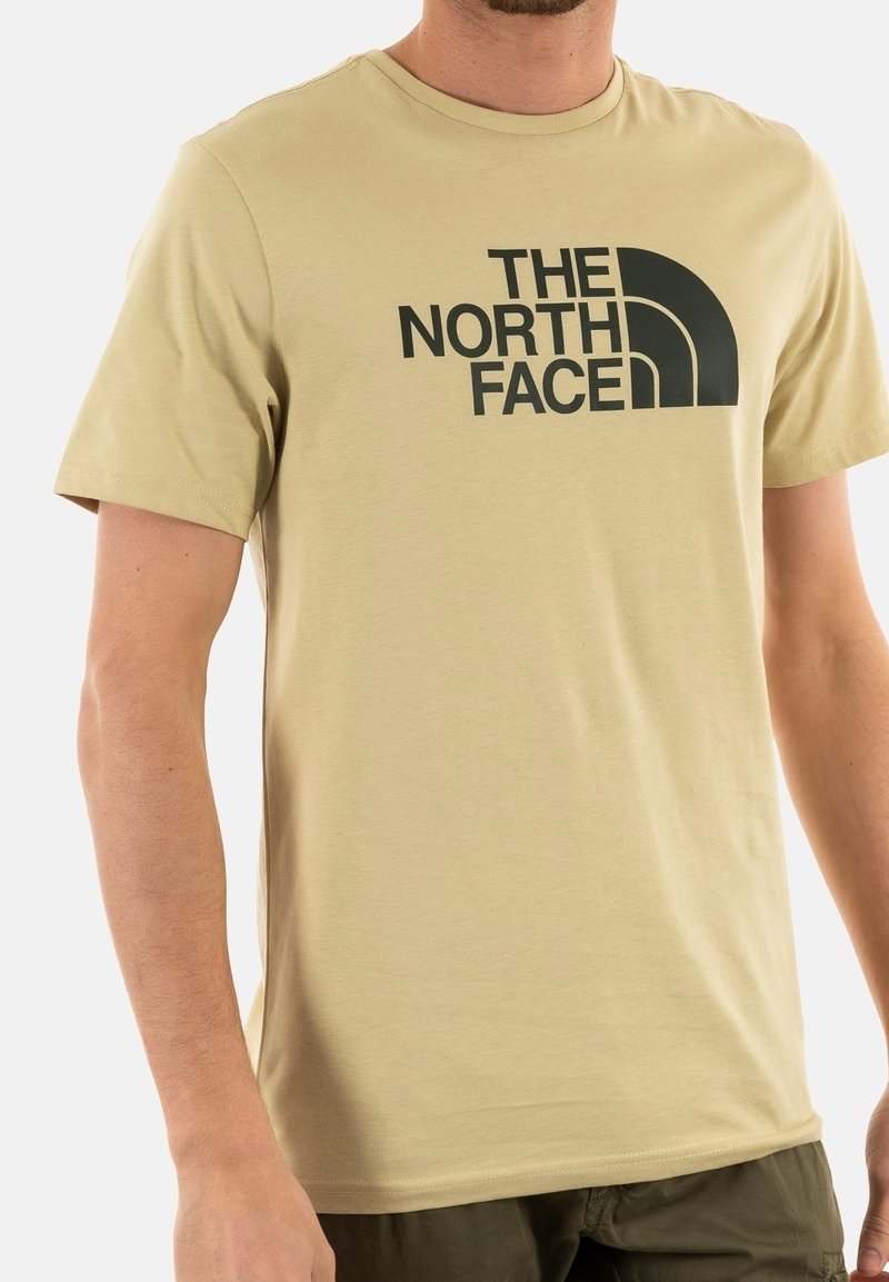 Beige bavlněné tričko s velkým černým logem "The North Face" na přední straně. Kulatý výstřih a krátké rukávy s hladkou texturou.