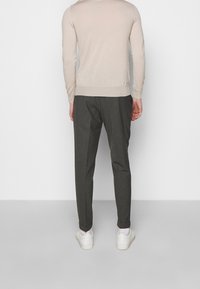 Světlé béžové svetřík s dlouhými rukávy, žebrovanými manžetami a lemem, zkombinovaný s tmavě šedými kalhotami a bílými teniskami. Zadní pohled.