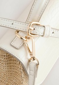 Borsa bianca realizzata in materiale sintetico con texture a coccodrillo e dettagli in paglia. Caratterizzata da hardware in tonalità oro e una tracolla regolabile con dettagli di cucitura.