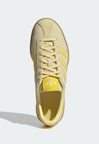 Keltaiset mokkasiinivetoketjut, joissa on kolme keltaista raitaa, pyöreä kärki, teksturoitu pinta ja vaalea kumipohja. Varustettu nauhoilla ja logolla kielessä.