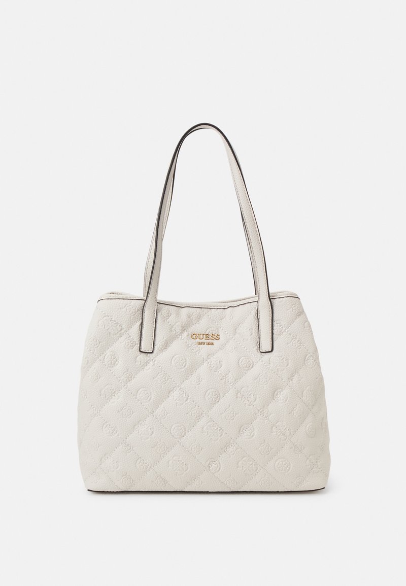 Sac d'épaule matelassé couleur crème avec motif embossé, doubles poignées bordées noir et un logo doré "Guess est 1981" au centre avant.