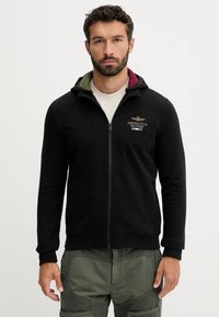 Felpa nera con zip in misto cotone con cappuccio a doppio strato caratterizzato da accenti verdi e bordeaux. Logo ricamato sul petto.