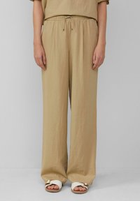 Beige wijde broek met een elastische taille en trekkoord, gemaakt van lichtgewicht stof, gecombineerd met witte sandalen met een gouden accent.
