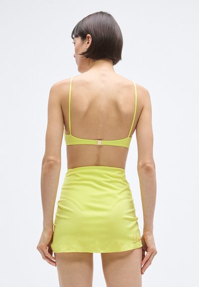 Sárga kétdarabos fürdőruha készlet, amely minimalistán tervezett, vékony pántokkal, mély kivágású hátrésszel, valamint hozzáillő, fodros textúrájú mini szoknyával.