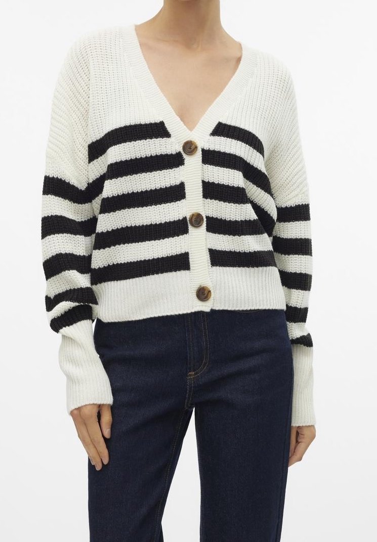 Cardigan en tricot blanc avec des rayures horizontales noires, boutons en bois, porté avec un jean bleu foncé sur une personne debout.